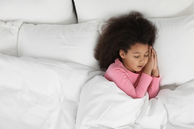 Photo of Cute little African-American girl sleeping in bed, top view