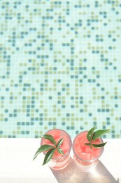 Photo of Refreshing watermelon drink in glasses near swimming pool outdoors, top view. Space for text