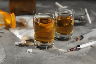 Photo of Alcohol and drug addiction. Whiskey in glasses, syringes, pills and cocaine on grey table, closeup