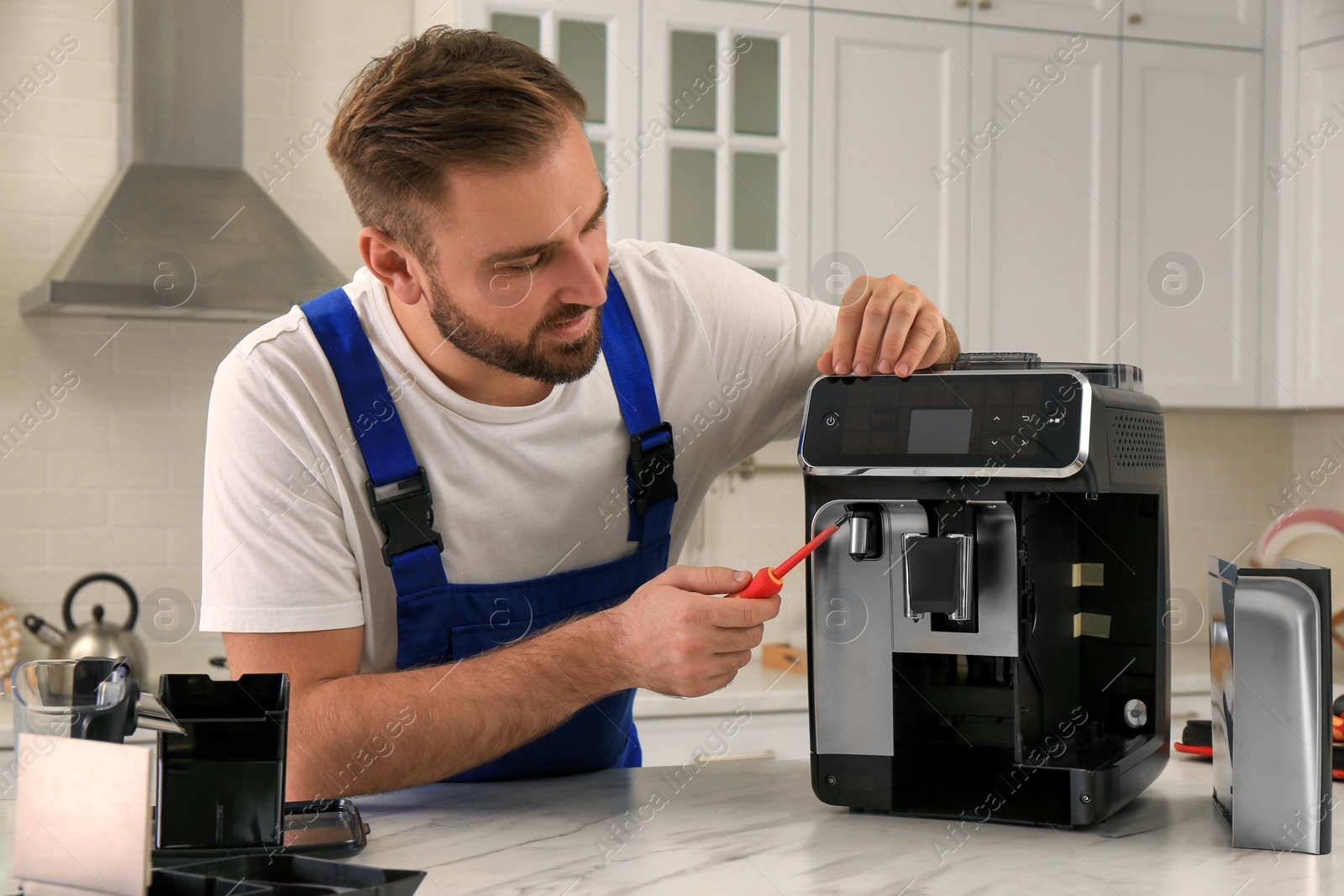 Photo of Repairman with screwdriver fixing coffee machine at table in kitchen