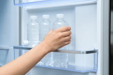 Woman taking bottle of water from refrigerator, closeup