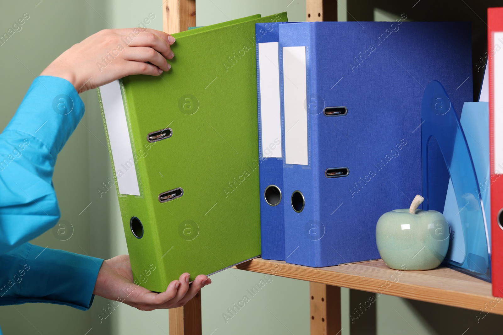 Photo of Woman taking binder office folder from shelving unit indoors, closeup