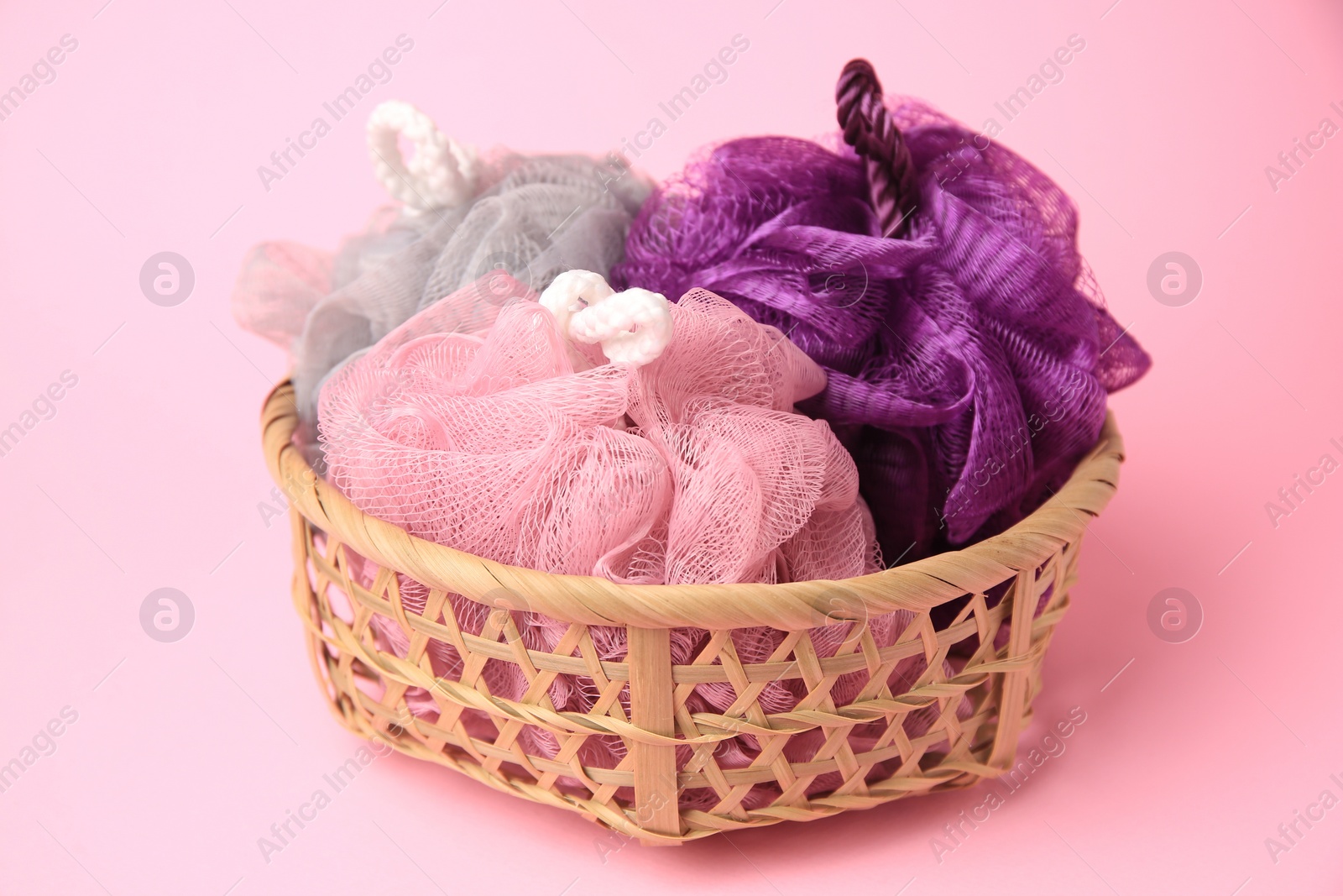 Photo of Wicker basket with colorful shower puffs on pink background