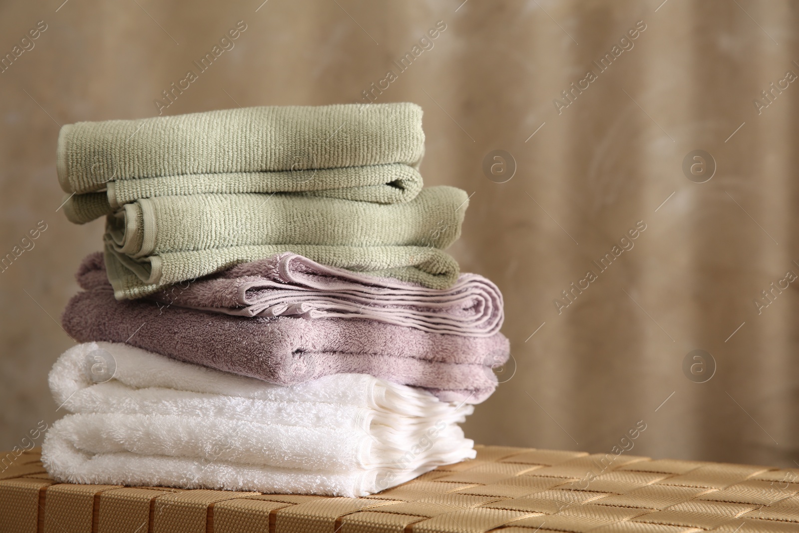 Photo of Stack of soft towels on wicker bench indoors, closeup. Space for text