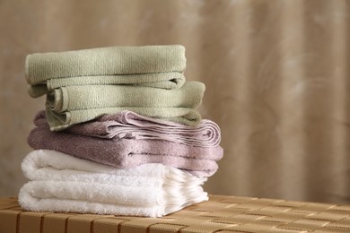 Photo of Stack of soft towels on wicker bench indoors, closeup. Space for text