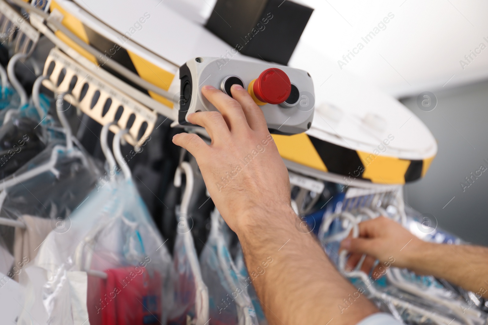 Photo of Worker pressing button on control panel of garment conveyor at modern dry-cleaner's, closeup