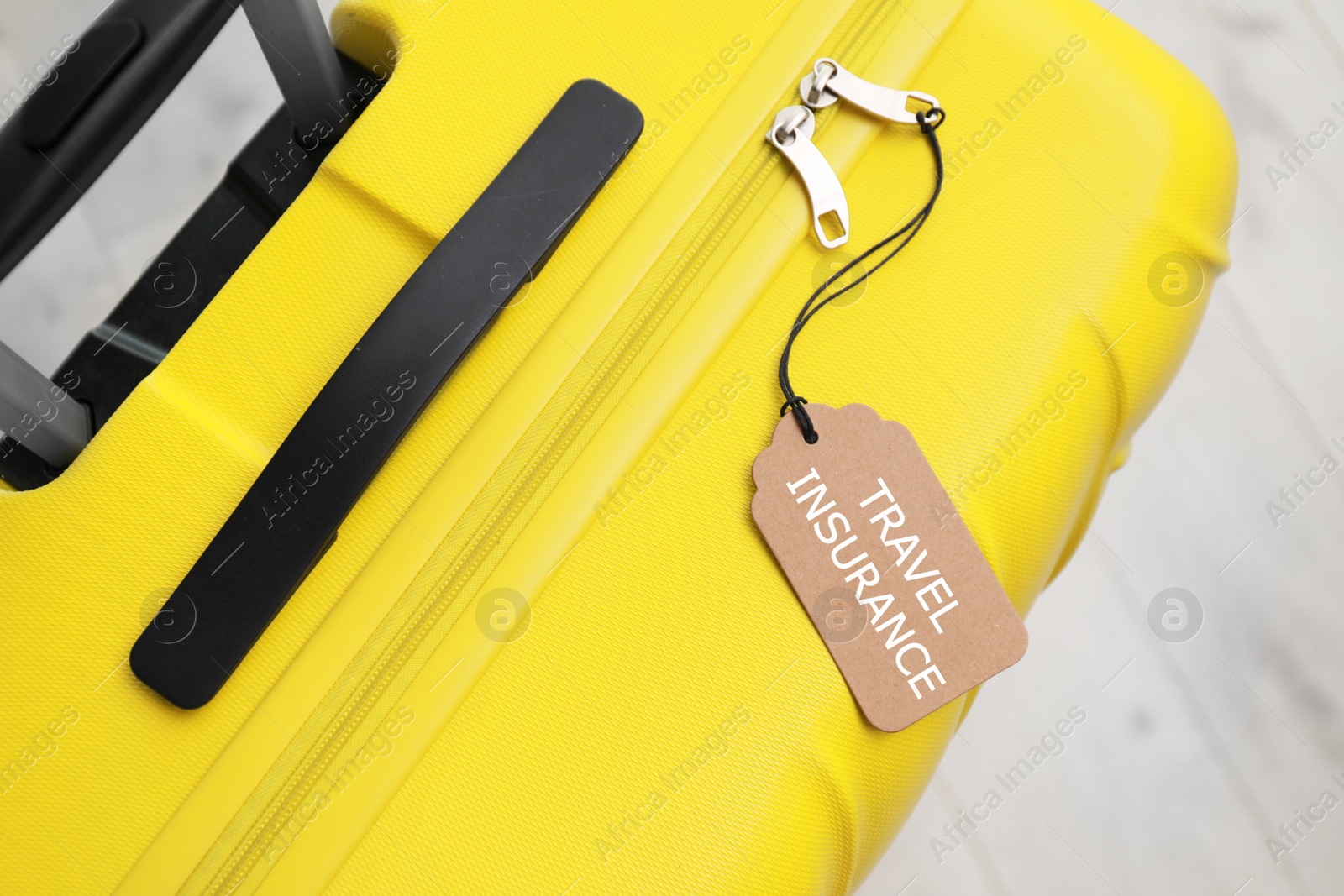 Photo of Yellow suitcase with TRAVEL INSURANCE label on floor, top view