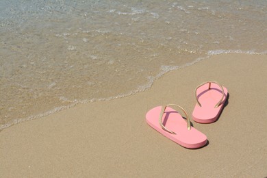 Photo of Stylish pink flip flops on wet sand near sea, space for text