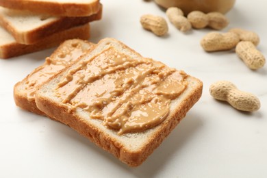 Photo of Delicious toasts with peanut butter and nuts on white table, closeup