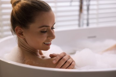 Photo of Beautiful woman taking bath in tub with foam indoors, closeup. Space for text