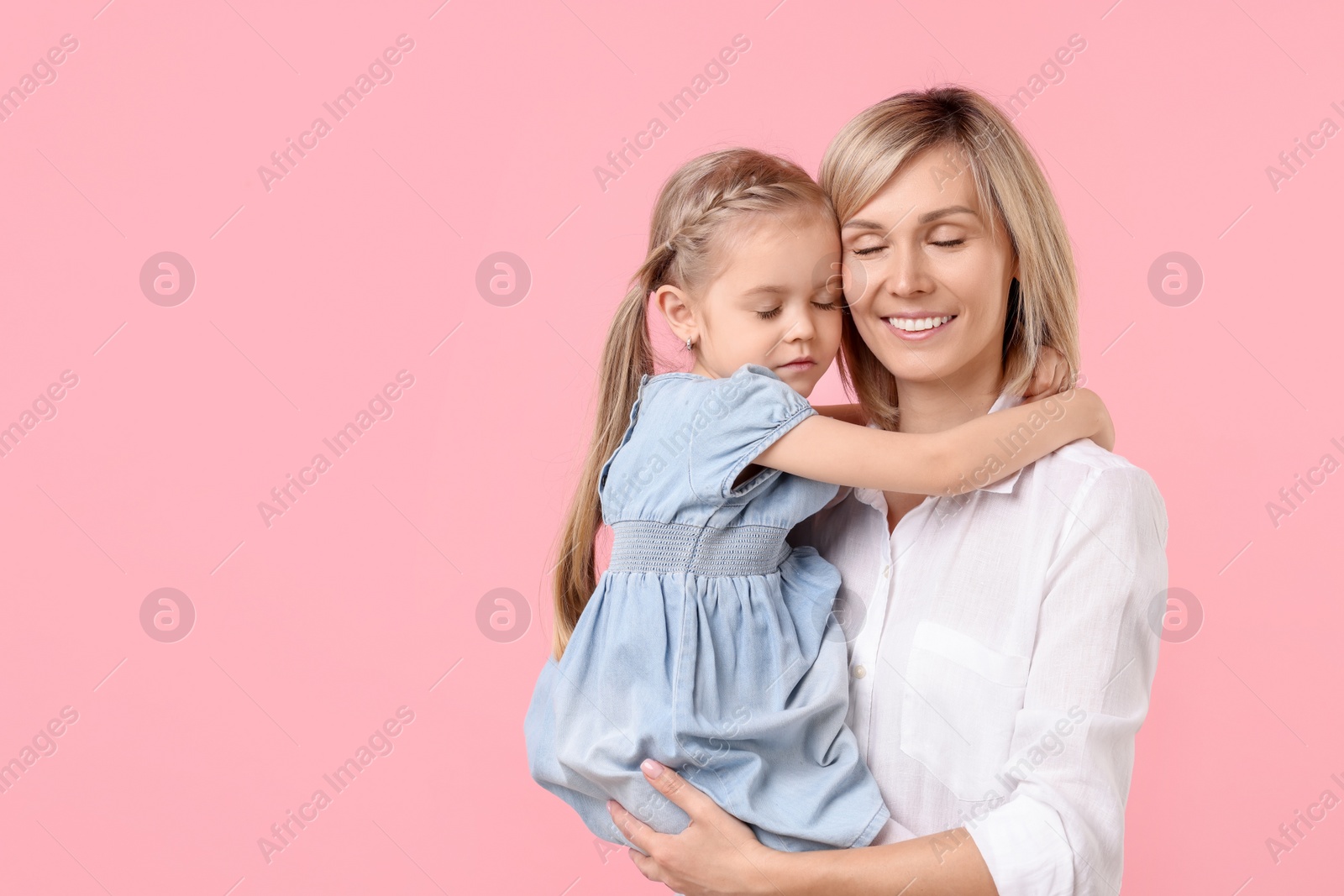 Photo of Daughter hugging and kissing her happy mother on pink background. Space for text