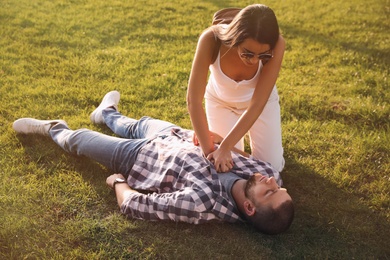 Photo of Woman doing cardiac massage to unconscious man with heart attack on green lawn