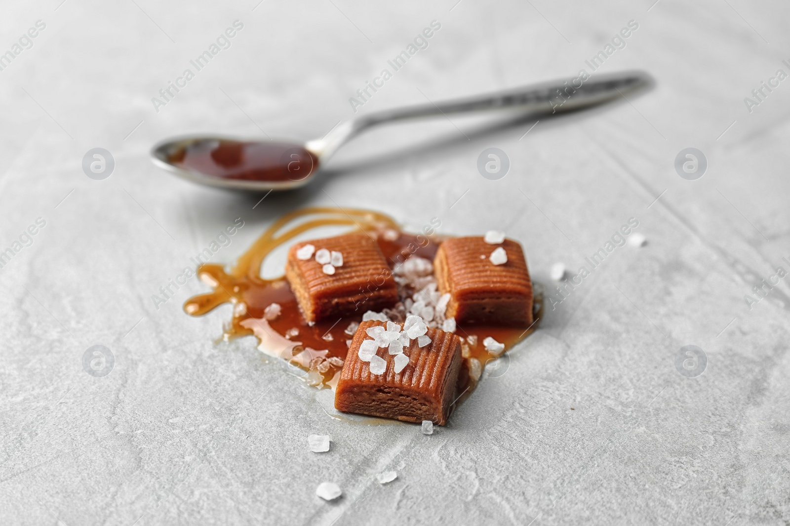 Photo of Delicious candies with caramel sauce and salt on light background