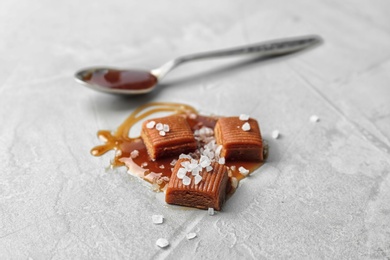 Delicious candies with caramel sauce and salt on light background