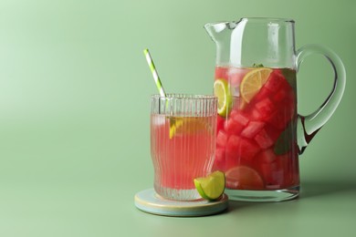 Photo of Tasty summer watermelon drink with lime in jug and glass on pale light green background. Space for text