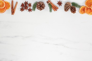 Dry orange slices, cinnamon sticks, fir branches and anise stars on white marble table, flat lay with space for text