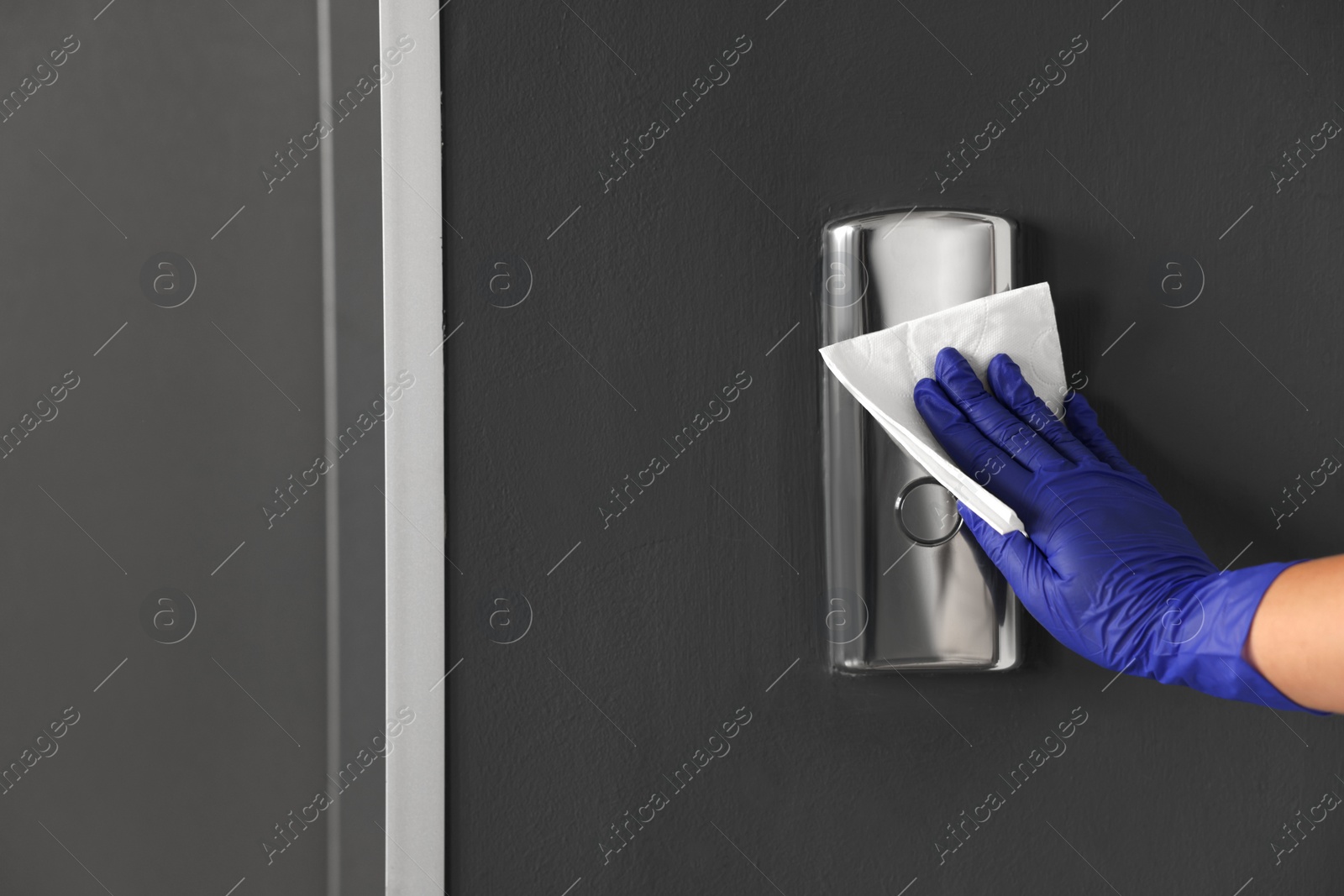 Photo of Woman wiping elevator call panel with paper napkin, closeup