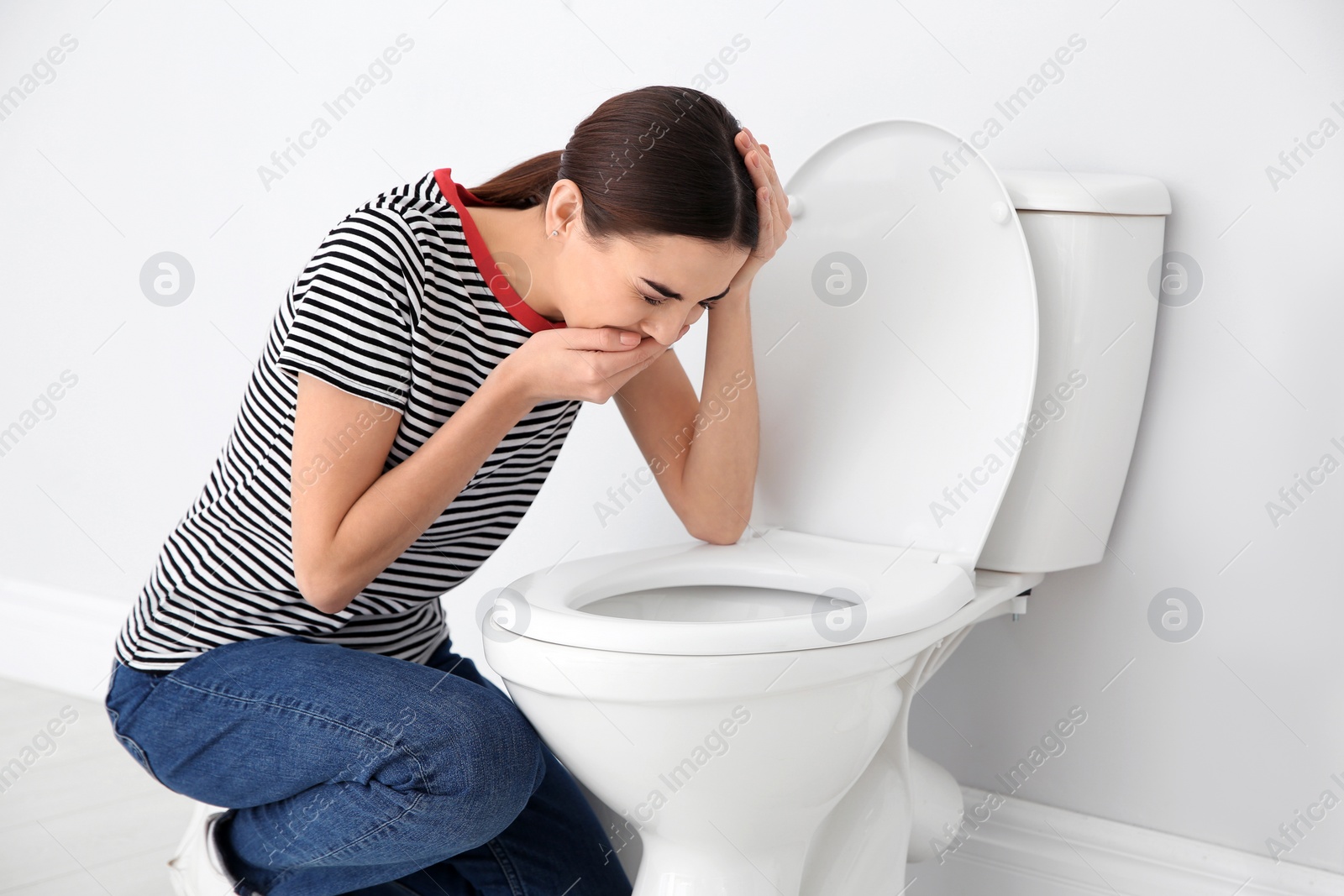 Photo of Young woman suffering from nausea over toilet bowl indoors