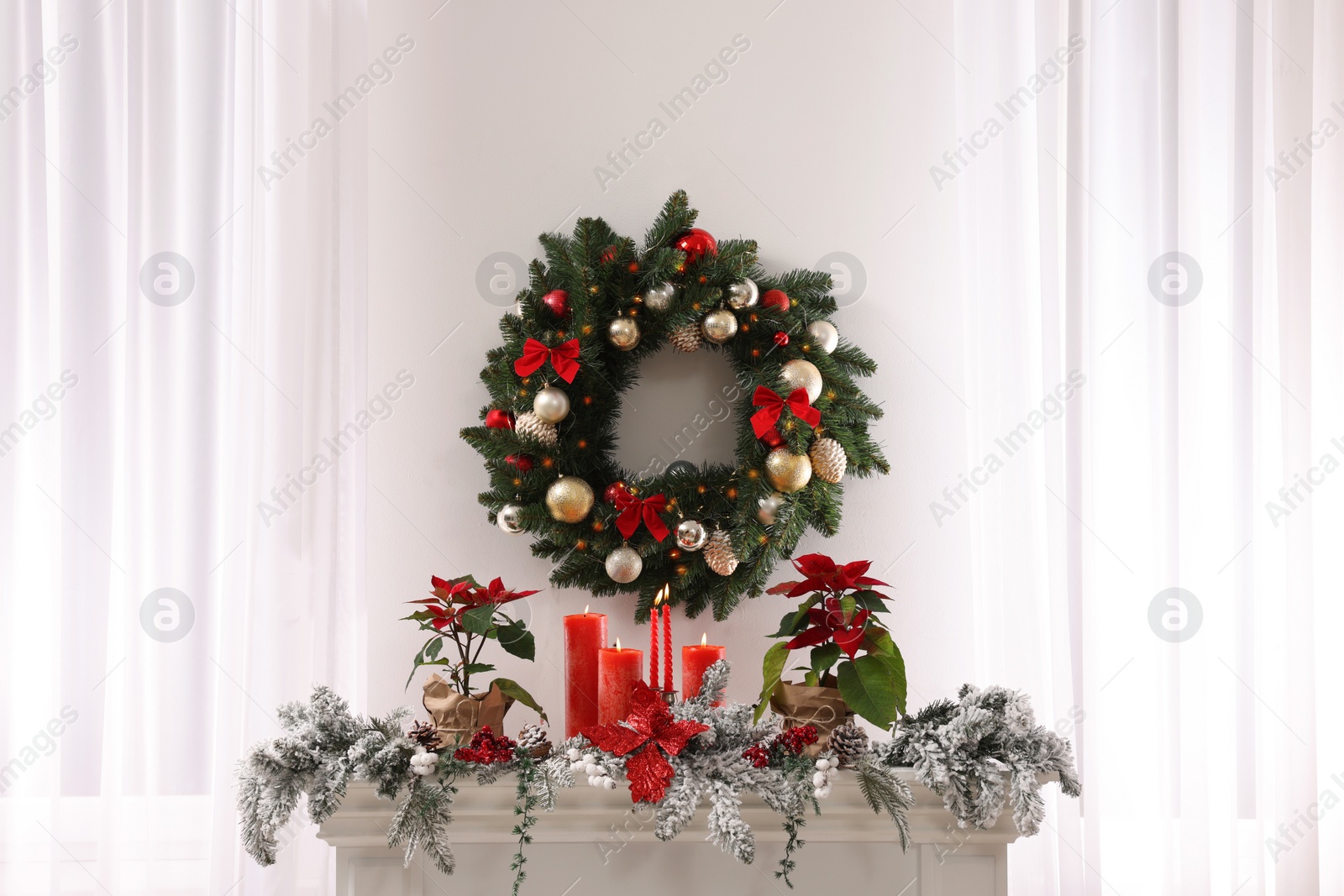 Photo of Beautiful Christmas wreath on white wall over decorated mantelshelf indoors