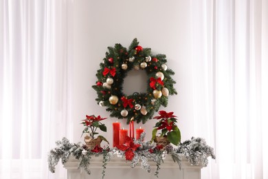 Photo of Beautiful Christmas wreath on white wall over decorated mantelshelf indoors
