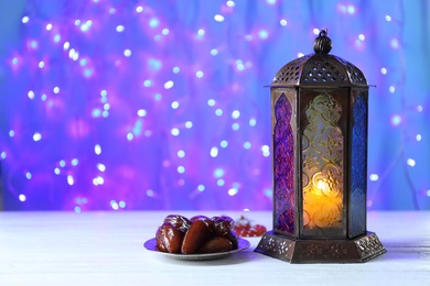 Photo of Composition with Muslim lamp on table against blurred lights. Fanous as Ramadan symbol