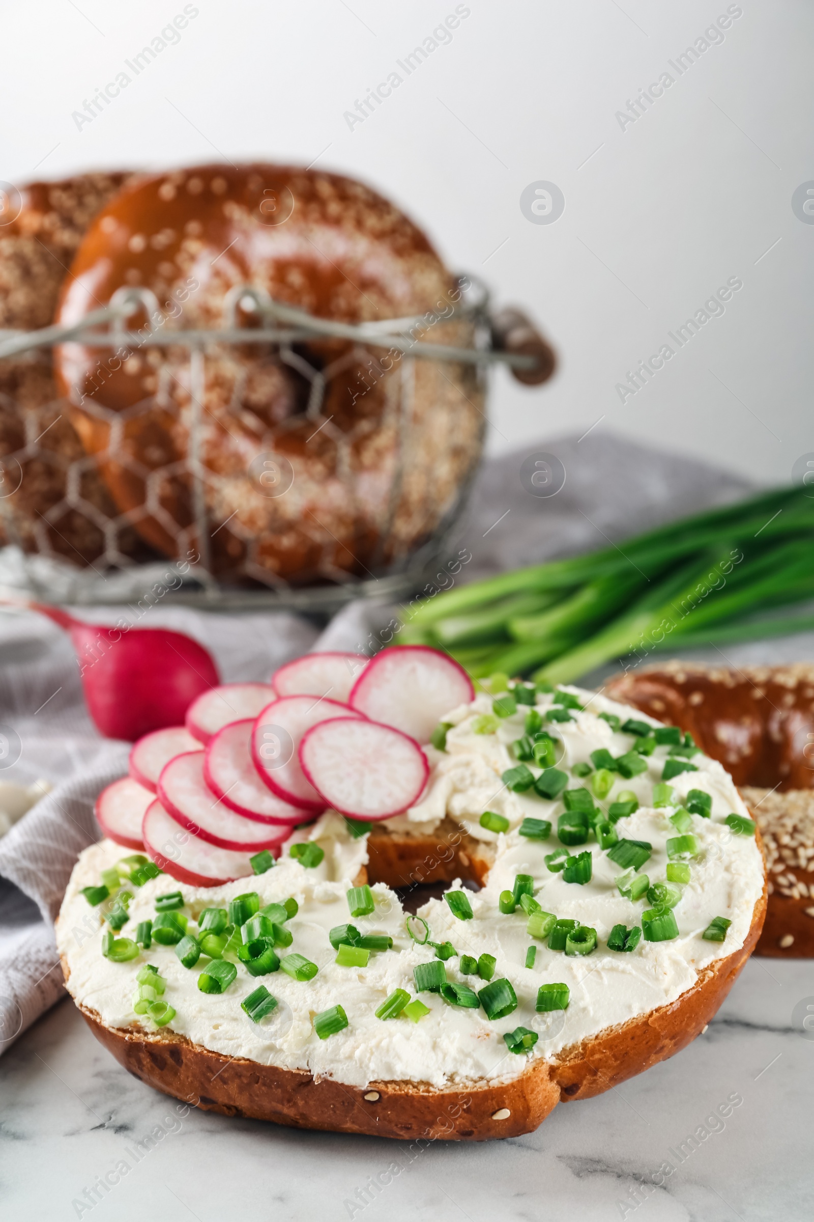 Photo of Delicious bagel with cream cheese, radish and green onion on white marble table