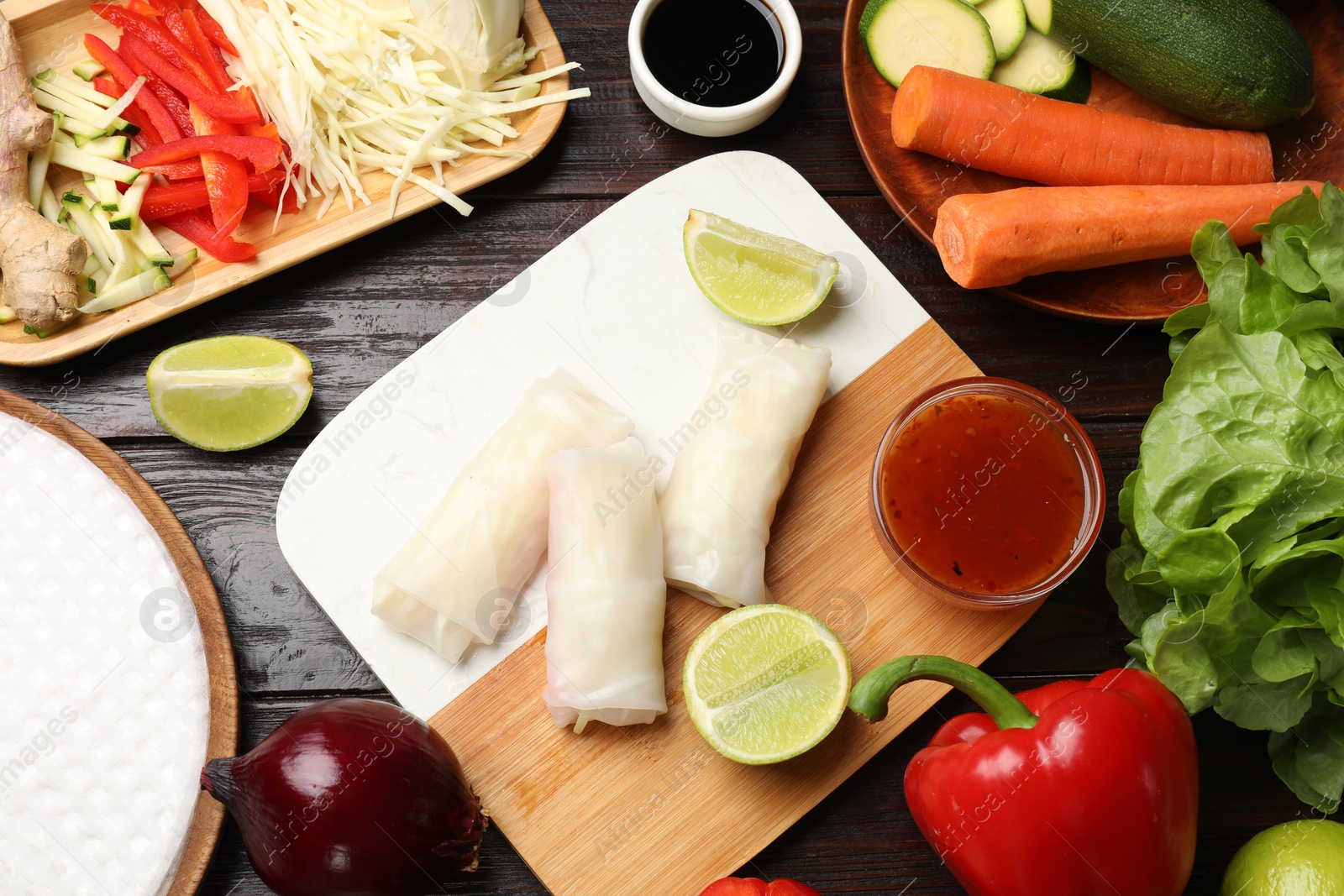 Photo of Delicious spring rolls with vegetables, lime and sauces on wooden table, flat lay