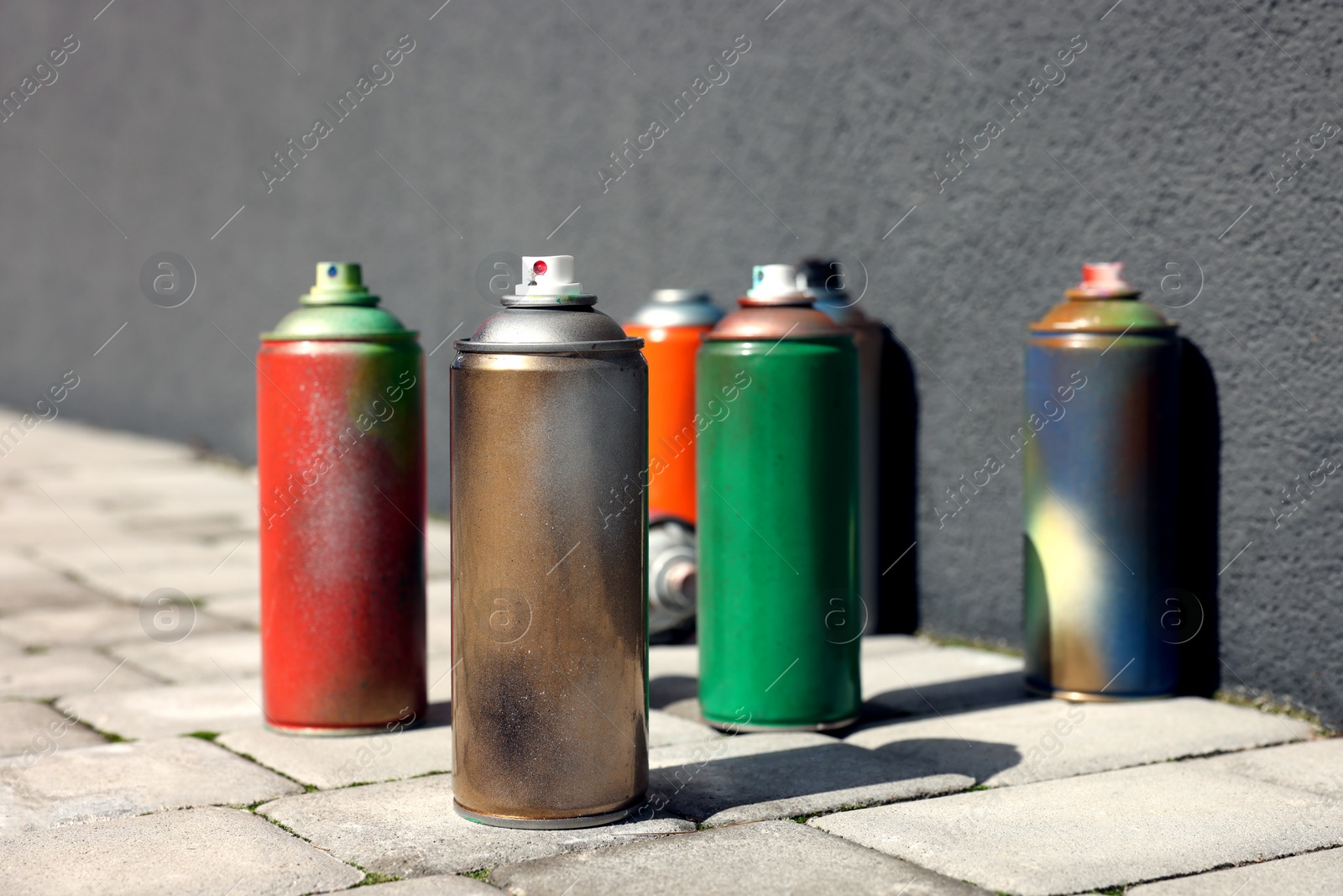 Photo of Cans of different spray paints on pavement near wall