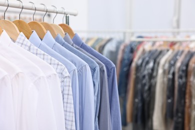 Photo of Dry-cleaning service. Many different clothes hanging on rack indoors, closeup