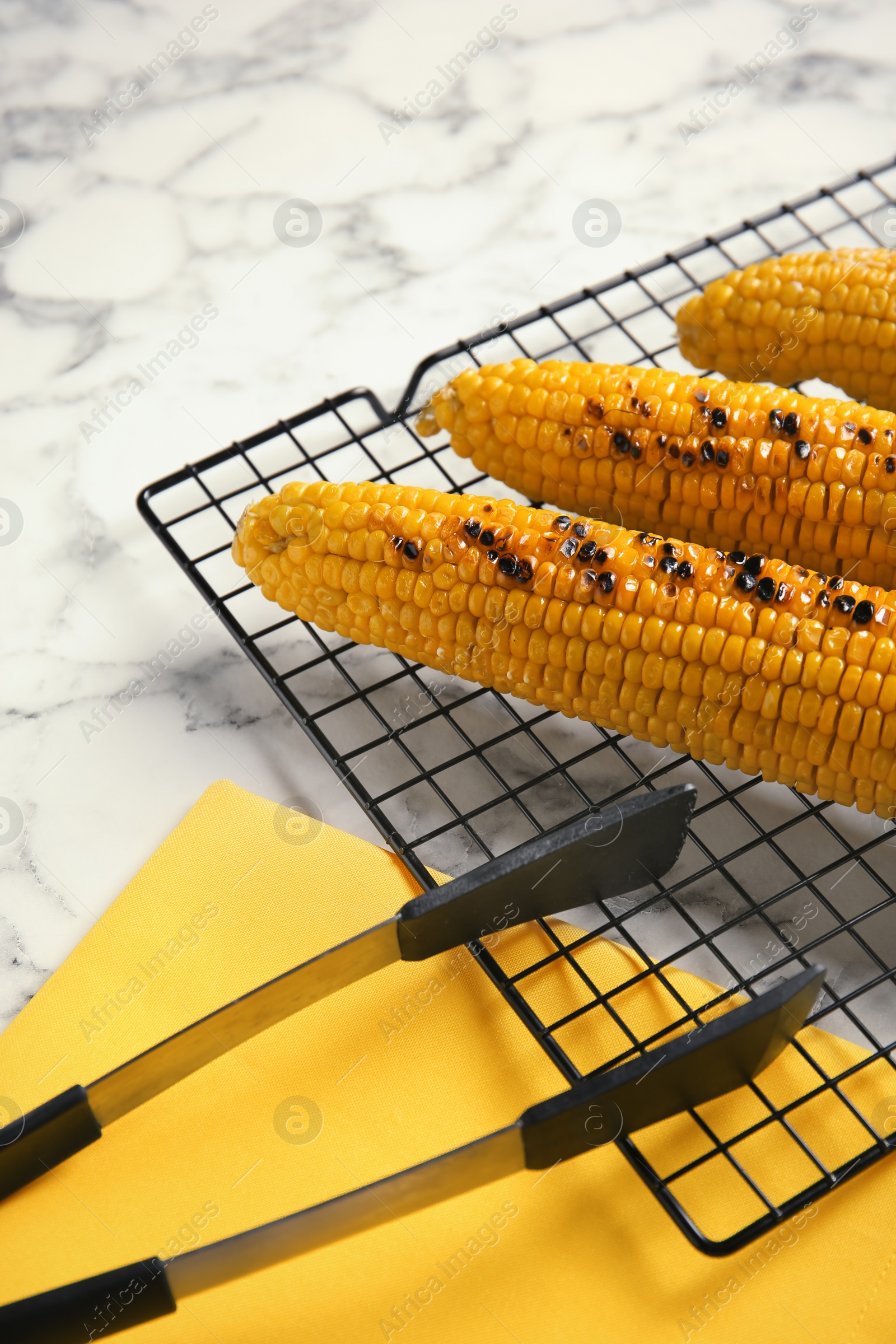 Photo of Cooling rack with grilled corn cobs on marble background