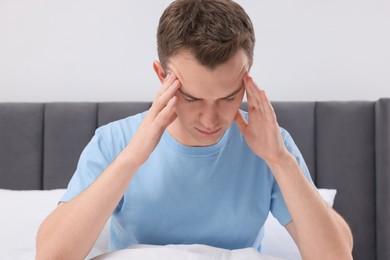 Photo of Sad man suffering from headache in bed indoors