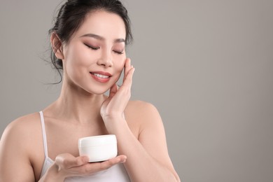 Happy woman applying face cream on grey background, space for text