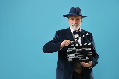 Senior actor holding clapperboard on light blue background, space for text. Film industry