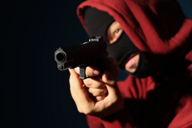 Photo of Man in mask holding gun on dark background, focus on hands