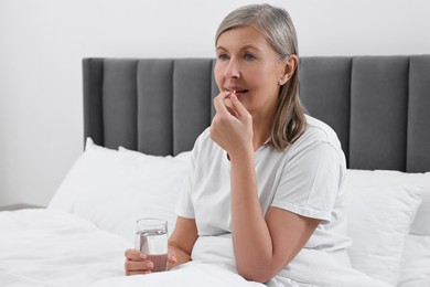 Beautiful woman taking vitamin pill in bedroom