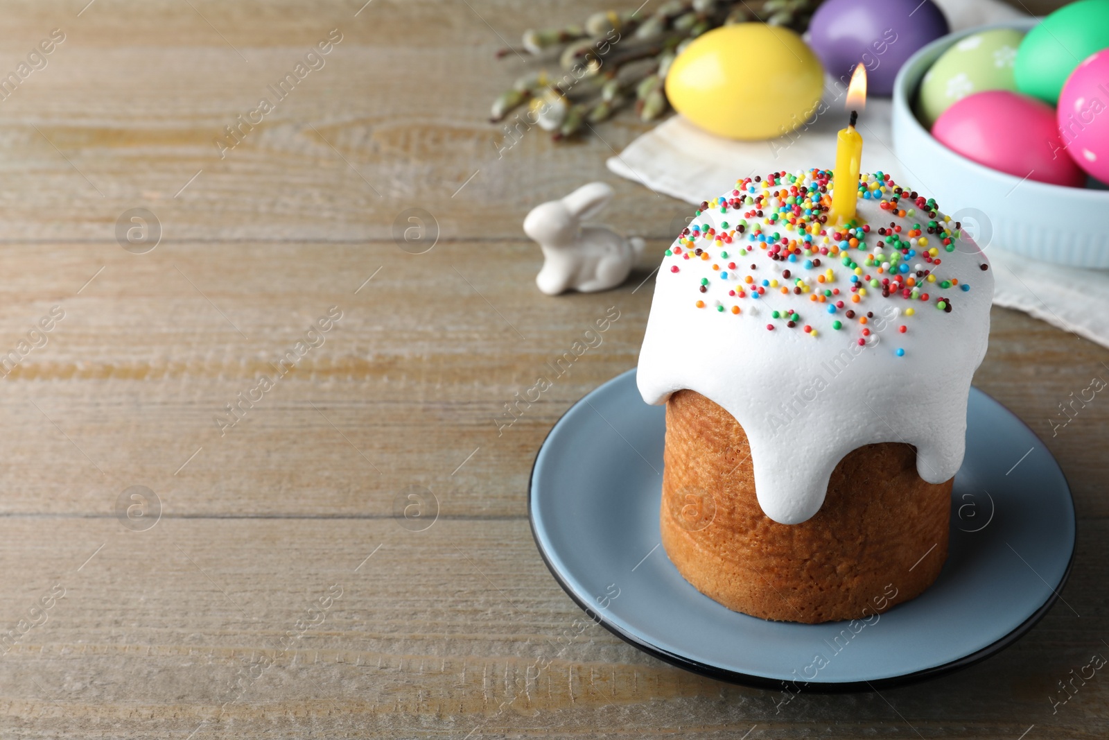 Photo of Easter cake with burning candle on wooden table, space for text