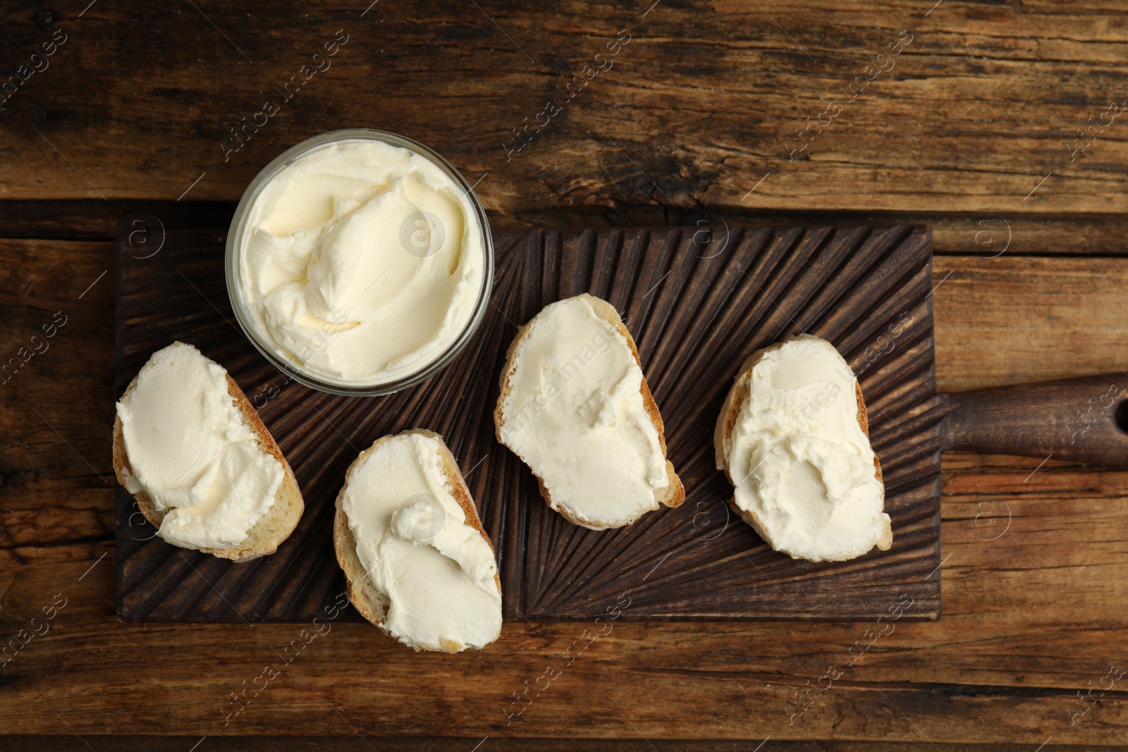 Photo of Bread with cream cheese on wooden table, top view
