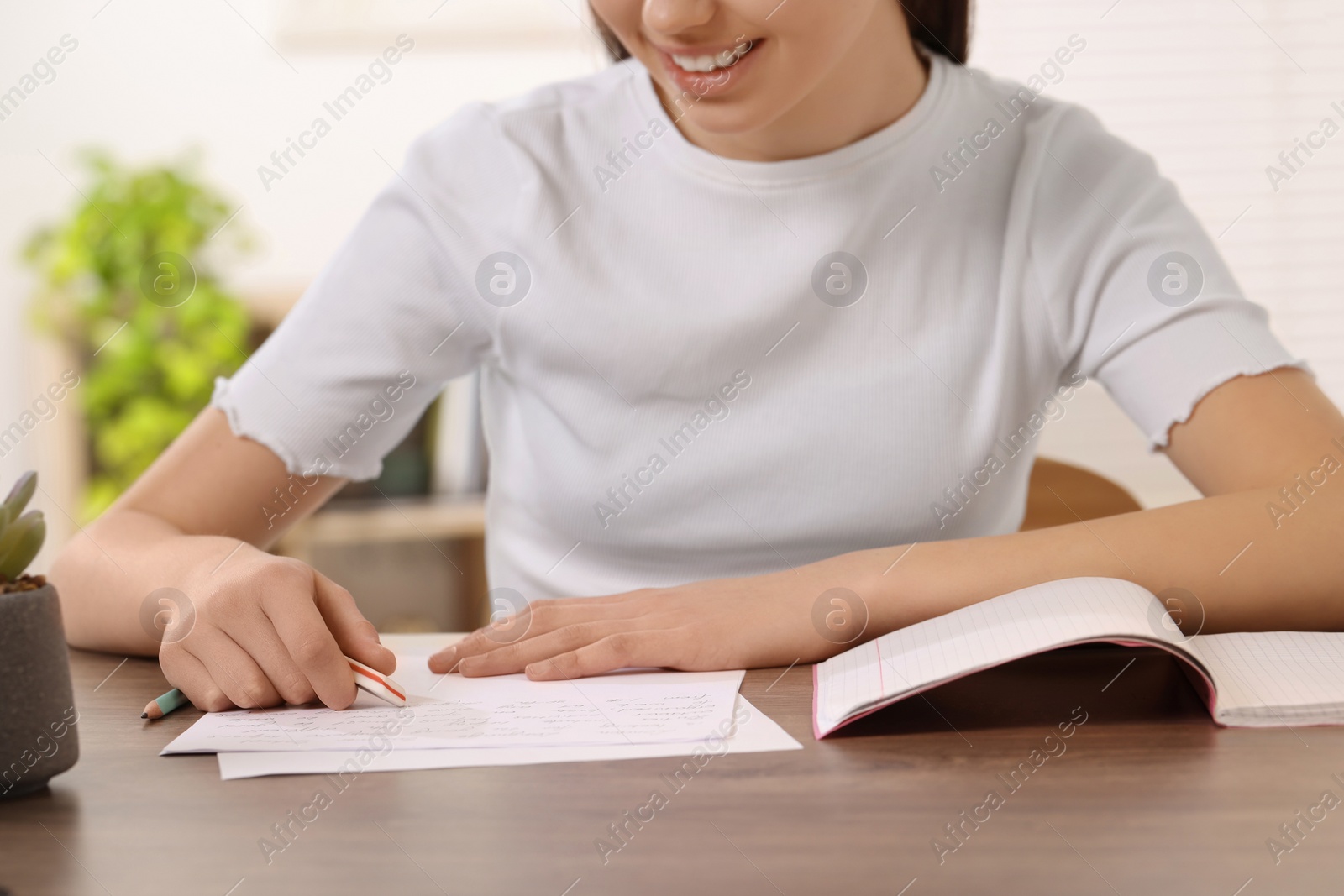 Photo of Teenage girl erasing mistake in her notebook at wooden desk indoors, closeup