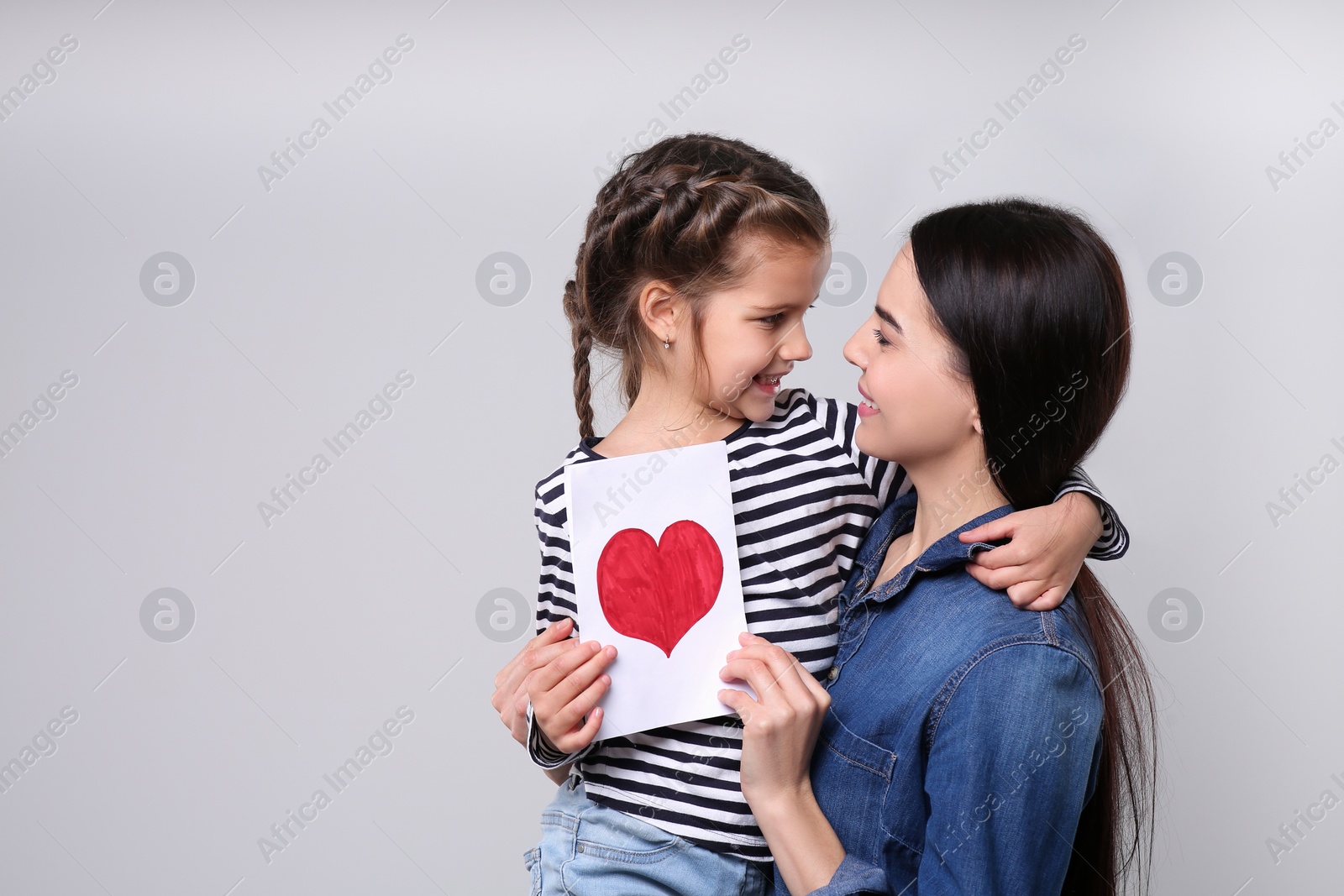 Photo of Happy woman with her daughter and handmade greeting card on light grey background, space for text. Mother's day celebration