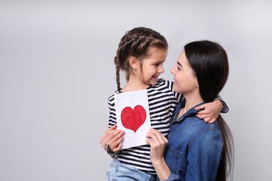 Photo of Happy woman with her daughter and handmade greeting card on light grey background, space for text. Mother's day celebration