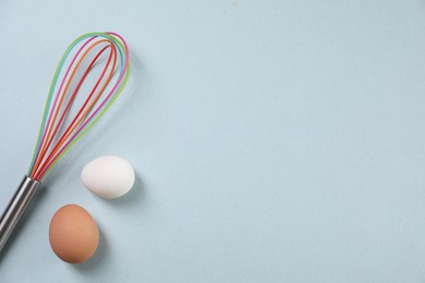Photo of Colorful whisk and raw eggs on light blue background, flat lay. Space for text