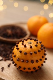 Photo of Pomander ball made of tangerine with cloves on wooden table against blurred festive lights, closeup