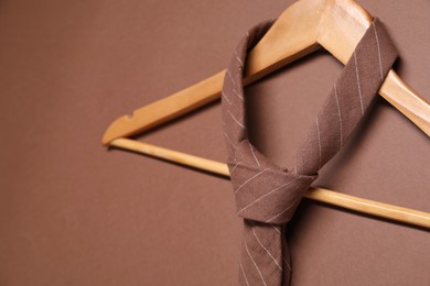 Photo of Hanger with striped necktie on brown background, closeup. Space for text