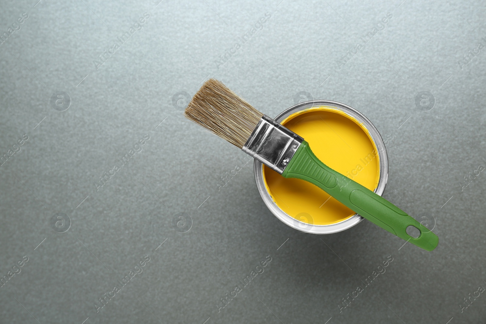 Photo of Can of yellow paint with brush on grey background, top view. Space for text