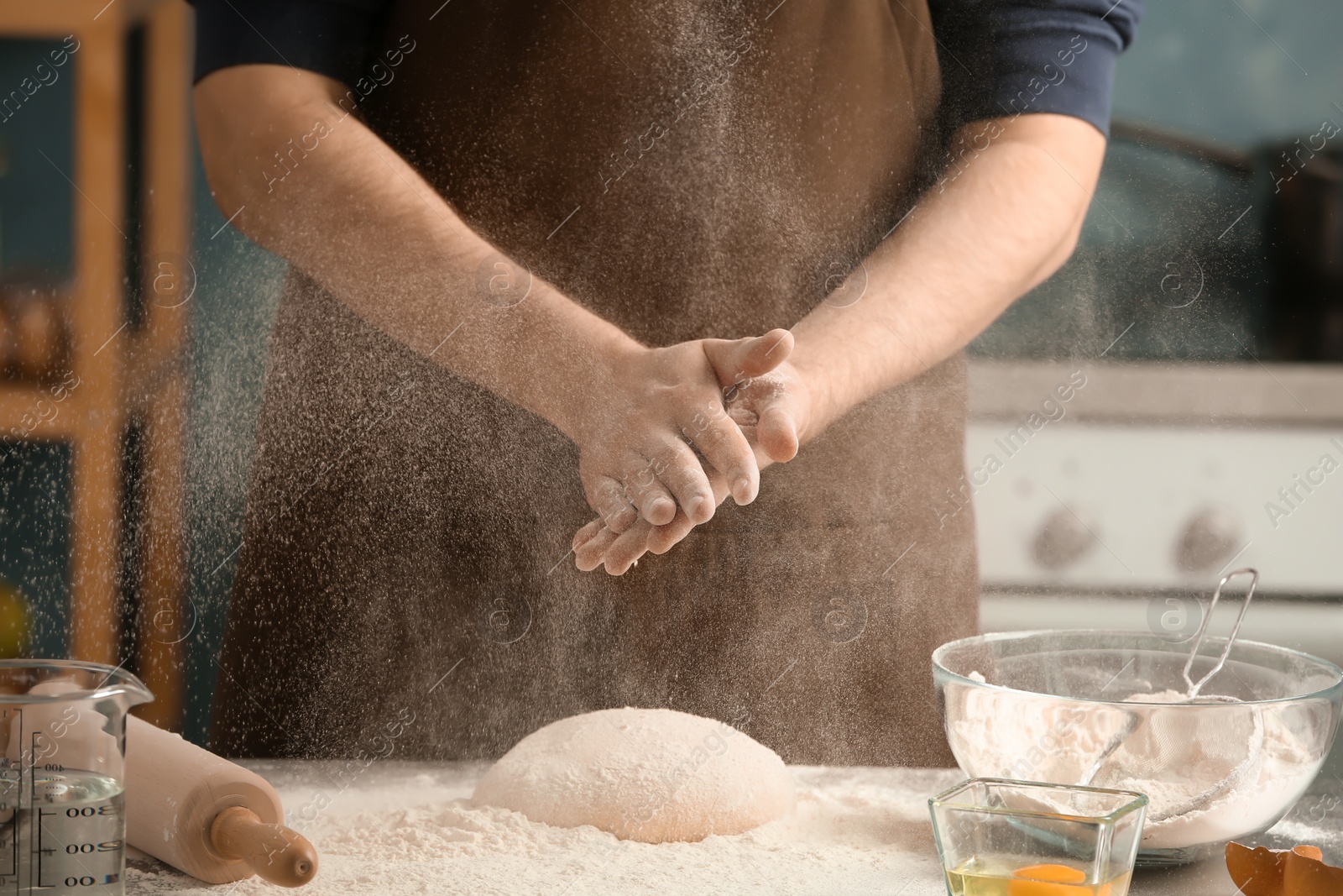 Photo of Man sprinkling flour over dough on table in kitchen