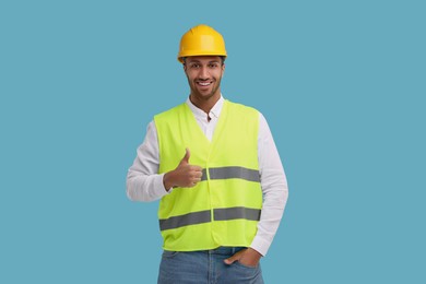 Photo of Engineer in hard hat showing thumb up on light blue background