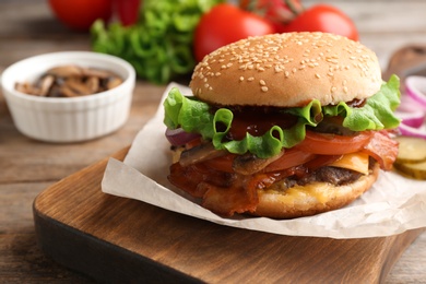 Photo of Tasty burger with bacon on wooden board, closeup