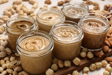 Photo of Many tasty nut butters in jars and nuts on table, closeup