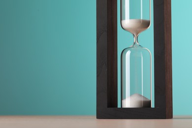 Hourglass with flowing sand on table against light blue background, space for text