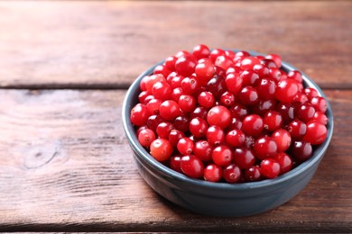 Photo of Fresh ripe cranberries in bowl on wooden table, closeup. Space for text